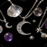 Composition élégante de bijoux ésotériques argentés avec lune, étoiles et pierres naturelles sur un velours noir.