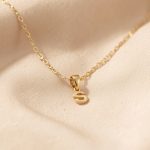 Bijoux spirituels : les porter avec élégance au quotidien Collier symbolique doré délicat disposé sur un tissu beige, photographié dans un style éditorial lumineux et élégant.