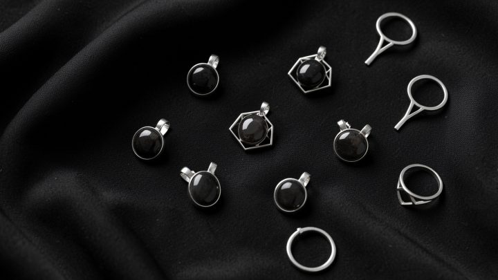 Vue de dessus de bijoux symboliques argentés ornés de pierres sombres, disposés avec élégance sur un tissu noir sous une lumière douce.