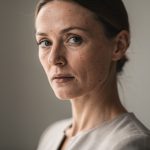 Portrait éditorial en trois quarts d’une femme adulte au visage expressif, éclairée par une lumière naturelle douce, dans une ambiance mode sobre et élégante.