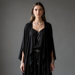 Femme portant une tenue noire bohème avec de délicats bijoux argentés inspirés des astres et des accessoires mystiques discrets, éclairée par une lumière éditoriale douce.